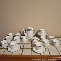 Full view of the coffee service set on tiled surface showing coffee pot, cream pitcher, sugar bowl, 12 cups and 12 saucers arranged.