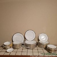 All pieces of the bone china dish set arranged in stacks on a tiled surface