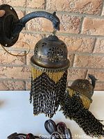 Pair of vintage wall sconces showing dark metal Art Nouveau style mounting arms and perforated domed metal shades with hanging black and gold beaded fringe.
