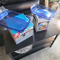 Photo showing two blue rectangular Pyrex baking dishes placed on top of Magic Bullet blender box and microwave cookware box on a black table.