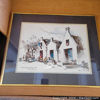 Framed artwork showing an exterior scene of the Schoongezich Wine Cellars with white buildings, blue shutters, figures, barrels, and trees.