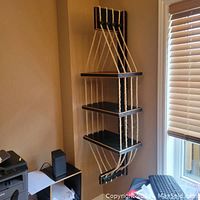 Front-left diagonal view of the wall hung shelving unit showing all three rope suspended shelves and back bracket attached to the wall with natural light from a window.