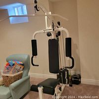 Full view of the white Wynne universal gym weight machine with black padded seats in a basement room, showing the weight stack and usage stations.