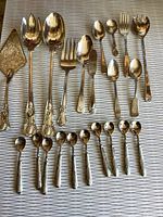 Photo showing 22 pieces of silver plated flatware laid out on a surface including large serving spoons, forks, small spoons, teaspoons, and a pie server.