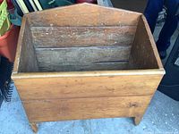 Front angled view of the wooden firewood box showing the rectangular shape, slanted back, and leg supports.