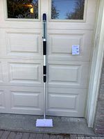 Full view of handheld car washing brush with extendable aluminum handle leaning against garage door.
