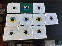 Overview of all 10 reggae 45 RPM vinyl records laid out on a dark surface, showing sleeves and labels.