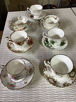 Top view of seven china cups and saucers arranged showing floral patterns and gold trim details.