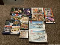 Photo of all sixteen boxed jigsaw puzzles laid out on carpet. Various colorful box artworks with winter scenes, animals, and landscapes.