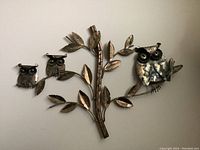 Metal wall decor showing three owls and detailed leaves on branches