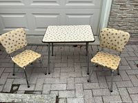 Full view of vintage children's table and two chairs, showing cream vinyl with small printed pattern and chrome legs.