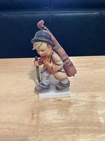 Side view of the West Germany ceramic figurine of a boy with mandolin and walking stick on a wooden surface.