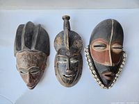 Overview of three vintage African masks showing different shapes, paint details, and adornments.