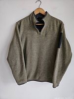 Front view of the Arc'teryx sweater on a wooden hanger with zipper partially down showing collar detail and fabric texture.