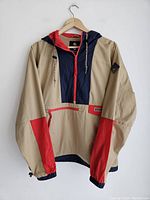 Full front view of Columbia windbreaker jacket on hanger showing beige, navy blue, and red color-block design.