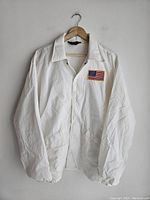 Full view of the vintage white jacket hanging on a wooden hanger showing front buttons and American flag patch on left chest.