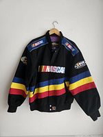 Front view of vintage NASCAR JH Design black jacket with blue, yellow, and red stripes, multiple NASCAR logos embroidered on chest and shoulders.