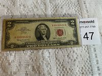 Front view of a 1963 Red Seal two-dollar bill on a white lace tablecloth, showing red seal and serial numbers with portrait of Thomas Jefferson.
