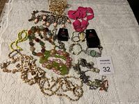 Full spread of costume jewelry including necklaces, bracelets, and earrings laid on white lace fabric.