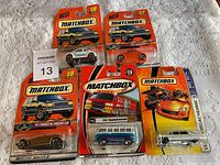 Five Matchbox cars in original sealed blister packaging on a fabric background with lot number sticker visible.