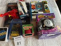 Miscellaneous lot displayed on white tablecloth including Magic 8 Ball, Captain America hammer pen, digital camera, card games, and toy gun.