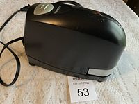 Side angled view of black Bostitch electric stapler with power cord, placed on white textured surface with lot number visible.