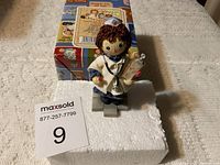 Front and angled close-up views of the Raggedy Ann nurse figurine showing details and original box behind, placed on white styrofoam block.