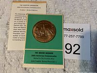 Photo of the bronze commemorative medal mounted in green folder with descriptive text and an insert about the Boston Massacre.