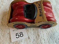 Front angled view of the Green Toys red race car in original cardboard packaging, showing the black interior and molded details.