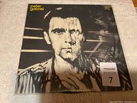 Front cover of Peter Gabriel vinyl album showing black and white stylized distorted portrait of the artist with yellow text.