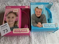 Pink and blue Vivitar headphones in original boxes showing front packaging with children models, placed on a white patterned surface.