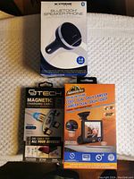 Photo showing all three boxed car accessories: magnetic charging cable, dual dash camera, and Bluetooth speaker phone