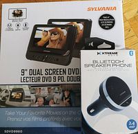 Boxed Sylvania 9" dual screen DVD player and Xtreme Auto Bluetooth speaker phone together.