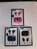 Front view of three Fisher ear pod sets in original packaging, one red and two black ear pods with charging cases.