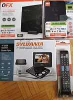 Top-down photo of four boxed electronics: two QFX HDTV antennas with 60 and 35 miles range respectively, Sylvania 7 inch portable DVD player with swivel screen, and a universal remote packaging.