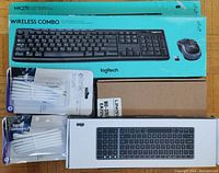 Photo showing three Logitech MK270 wireless combos in original blue boxes, one Linksys router, and six packaged white coaxial cables.