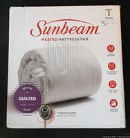 Photo of box front showing Sunbeam heated mattress pad in twin size with key features including 20 heat settings, selectable auto-off, easy wash and care, and preheat feature. Packaging shows some wear.