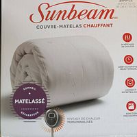 Front view of the folded white quilted mattress pad inside original Sunbeam packaging, showing dimensions and bilingual labeling