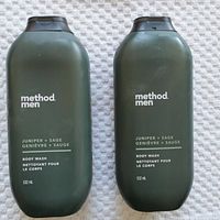 Two Method Men Juniper + Sage body wash bottles, olive green with black caps, labeled with text showing scent and volume.