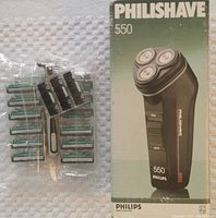 Philips Philishave 550 electric shaver with original retail box and multiple razor blades alongside manual razor in plastic packaging.