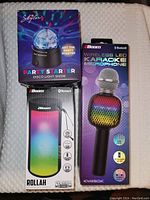 Photo showing original packaging of three party kit items: Skylar disco light bulb, 2Boom Rollah Bluetooth speaker, and 2Boom wireless LED karaoke microphone