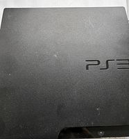Top view of black Sony PlayStation 3 console with visible PS3 logo and some light surface wear.