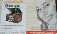 Close-up of the product box showing Sylvania branding, Bluetooth feature, wood finish and nostalgic design indications with model number SRCD838BT.
