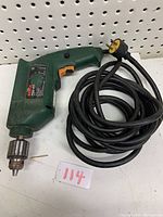 Green Bosch PSB40 drill with black and orange trigger, long cord coiled, hanging on pegboard.