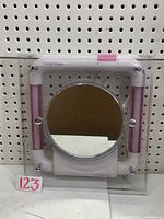 Square framed makeup mirror with round central mirror and two pink vertical light tubes on sides, mounted on pegboard.