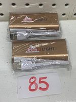 Two Coors Light branded gold power banks, each with USB cable in original plastic wrap, laid flat on surface