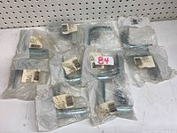 Lot of multiple zinc corner braces individually wrapped in clear plastic, arranged on a pegboard background.