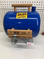 Blue Dad's Root Beer branded charcoal BBQ grill with wooden handles and metal stand.