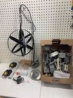 Black metal globe hanging pendant light with chain, two small sconce lights, several LED bulbs, and box of assorted electrical boxes and outlets displayed against a pegboard.
