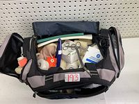 View of open gym bag showing various first aid supplies inside including scissors, tape rolls, gauze pads, and foam padding.